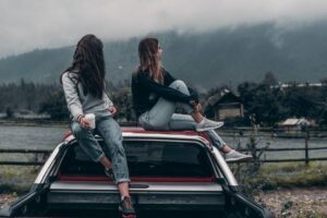 2 teenage girls sitting atop a car